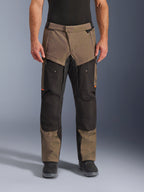 Alpinestars Cusco Drystar® Pants, motocyklowe spodnie turystyczne adventure touring, orzechowo-czarne z pomarańczowymi akcentami, widok z przodu na modelu, techniczna konstrukcja tekstylna, kieszenie cargo i zamki wentylacyjne, zestawione z czarnymi butami motocyklowymi