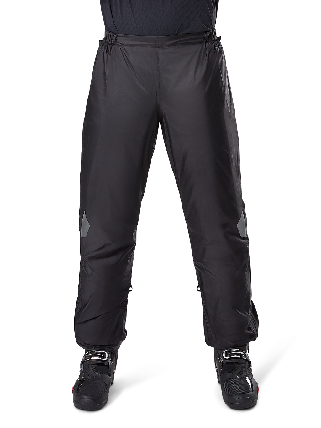 Alpinestars Bogota Pro Drystar 3 Seasons Pants, wodoodporne spodnie motocyklowe, czarne, lekka tkanina techniczna z odblaskowymi naszywkami na kolanach, noszone jako spodnie wierzchnie z czarnymi butami motocyklowymi, zaprojektowane dla ochrony przed warunkami pogodowymi w turystyce adventure