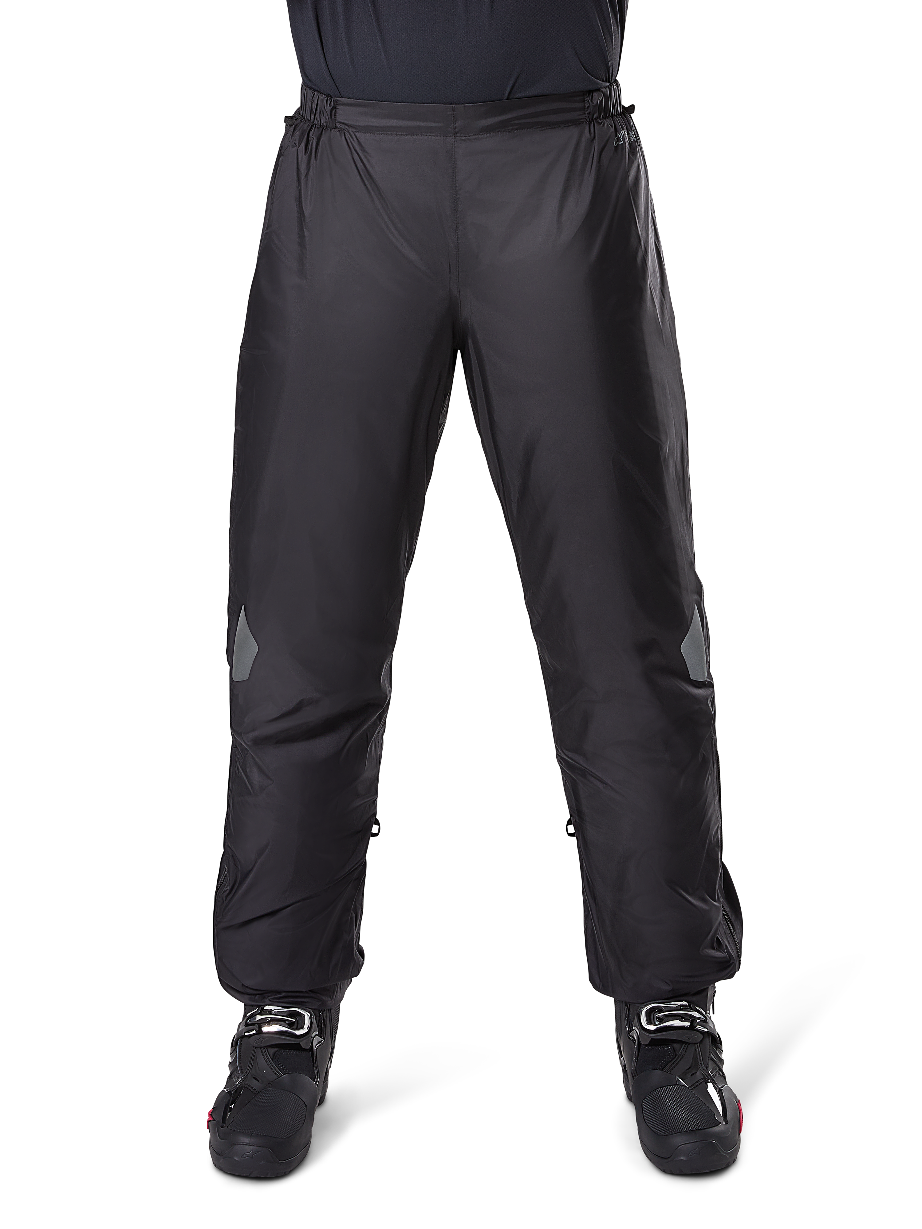 Alpinestars Bogota Pro Drystar 3 Seasons Pants, wodoodporne spodnie motocyklowe, czarne, lekka tkanina techniczna z odblaskowymi naszywkami na kolanach, noszone jako spodnie wierzchnie z czarnymi butami motocyklowymi, zaprojektowane dla ochrony przed warunkami pogodowymi w turystyce adventure
