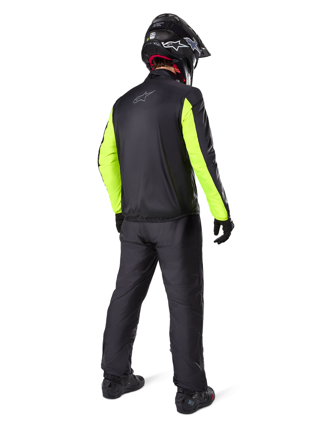 Motocyklista widziany od tyłu w czarnych spodniach Alpinestars Bogotá Pro Drystar® 3 Seasons, połączonych z czarną kurtką z neonowożółtymi rękawami, czarnym kaskiem adventure i butami, kompletny strój do turystyki przygodowej