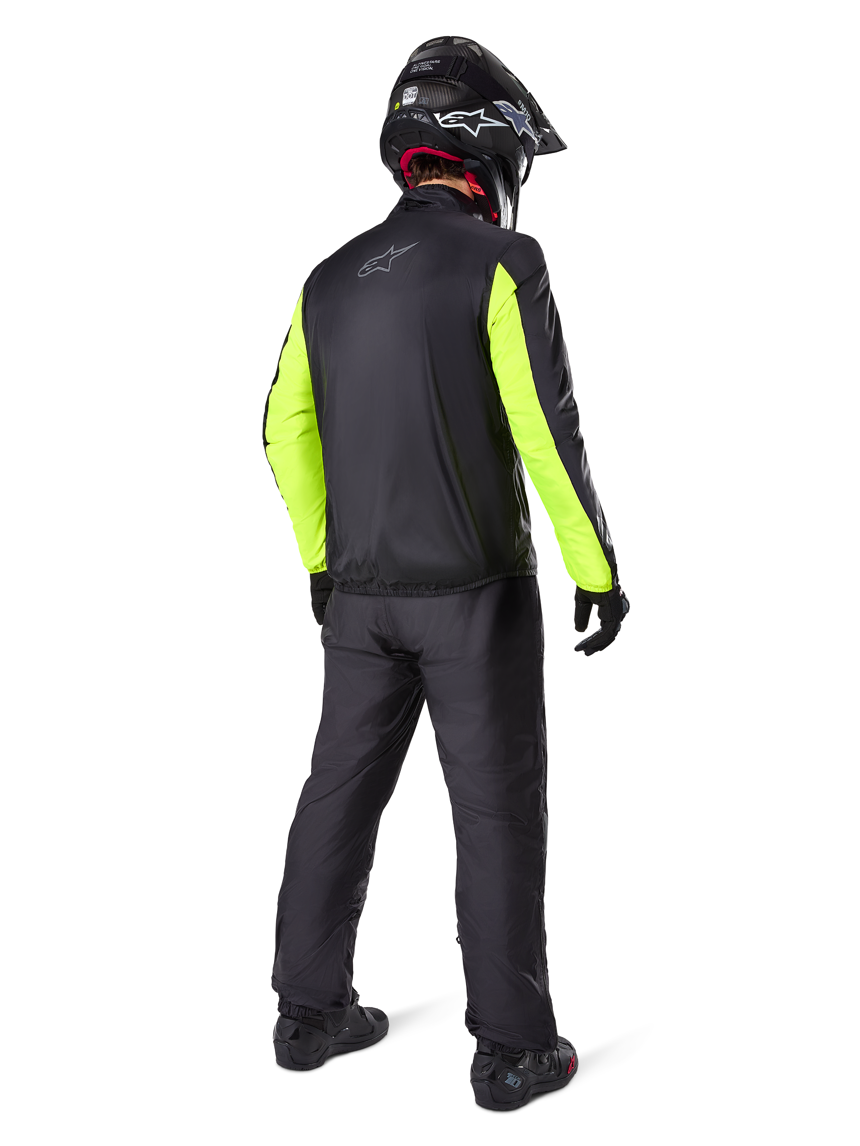 Motocyklista widziany od tyłu w czarnych spodniach Alpinestars Bogotá Pro Drystar® 3 Seasons, połączonych z czarną kurtką z neonowożółtymi rękawami, czarnym kaskiem adventure i butami, kompletny strój do turystyki przygodowej