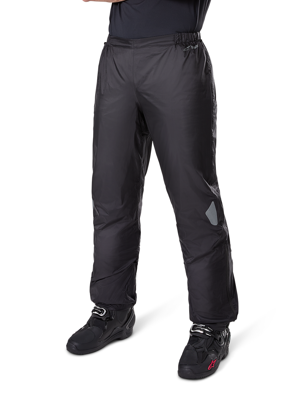 Spodnie Alpinestars Bogotá Pro Drystar® 3 Seasons, motocyklowe spodnie adventure touring, czarne, noszone z czarnymi butami motocyklowymi, z odblaskowymi naszywkami na kolanach i logo Drystar, lekka wodoodporna konstrukcja tekstylna do jazdy całorocznej
