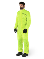Alpinestars Hurricane Rain V2 Suit, jednoczęściowy wodoodporny kombinezon motocyklowy, żółty fluo, noszony z czarnymi rękawicami i butami, czarne logo Alpinestars na klatce piersiowej, odblaskowe detale na nogawkach
