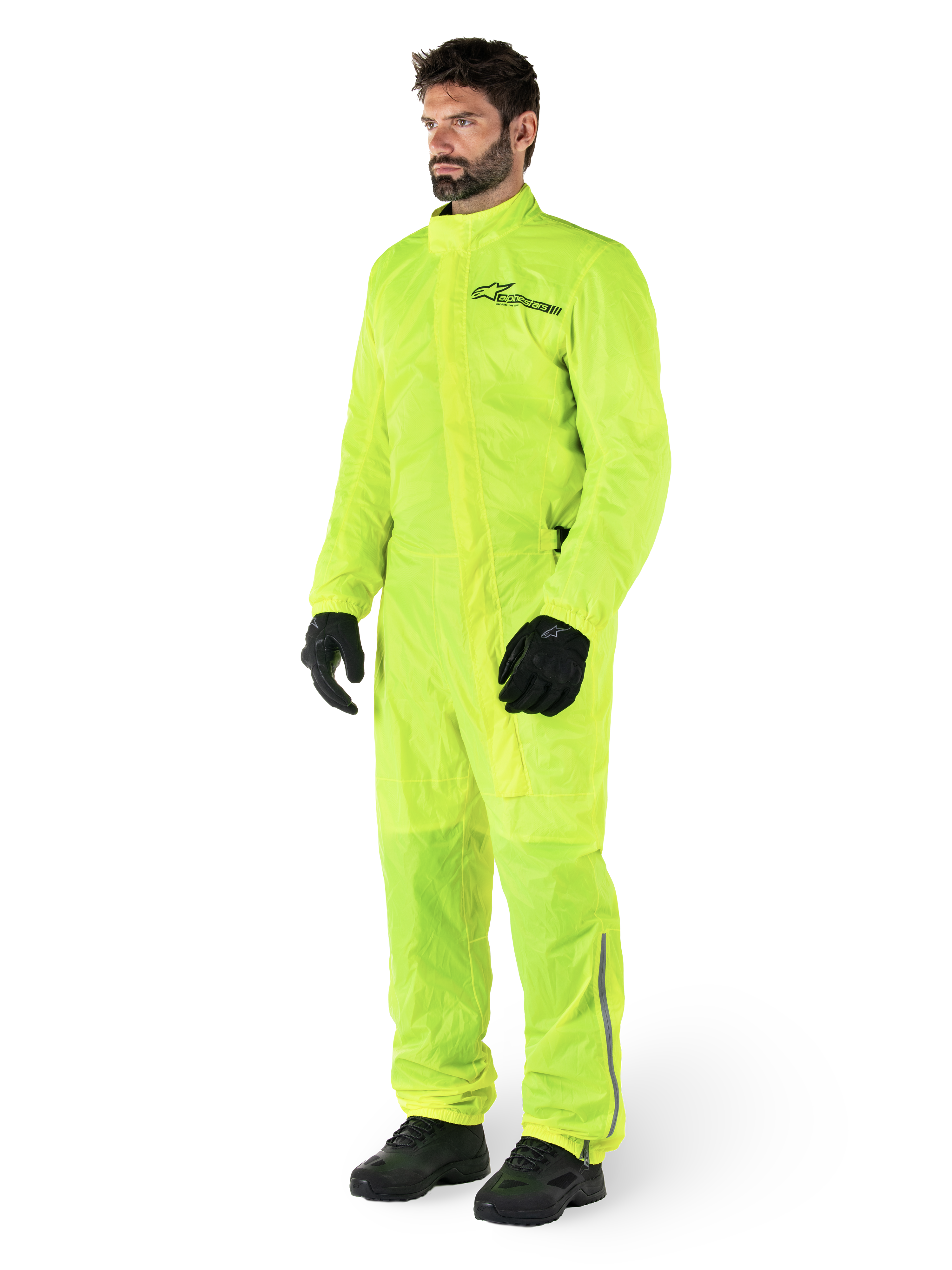 Alpinestars Hurricane Rain V2 Suit, jednoczęściowy wodoodporny kombinezon motocyklowy, żółty fluo, noszony z czarnymi rękawicami i butami, czarne logo Alpinestars na klatce piersiowej, odblaskowe detale na nogawkach