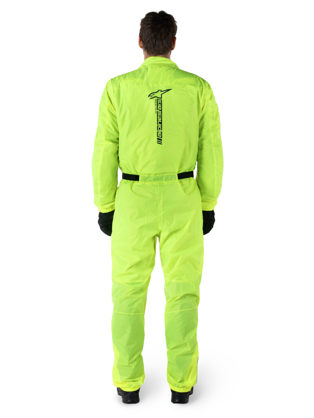 Alpinestars Hurricane Rain V2 Suit, jednoczęściowy motocyklowy kombinezon przeciwdeszczowy, żółty fluo, widok z tyłu z pionowym czarnym logo Alpinestars, elastyczny pas i mankiety, noszony z czarnymi rękawicami i butami, wodoodporna i wiatroodporna odzież motocyklowa