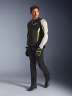 Alpinestars AST V3 Air Jacket, lekka tekstylna kurtka motocyklowa w kolorach czarnym, srebrnym i żółtym fluo, noszona przez modela z czarnymi spodniami i dopasowanymi rękawicami, wyposażona w panele z siatki i perforacje laserowe do sportowej jazdy w ciepłe dni.