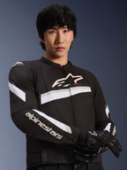 Alpinestars T-GP Plus R V4 Jacket, Black and White, worn by a male model, textile motorcycle jacket with white stripes across the chest and sleeves, Alpinestars logo on the chest, paired with black riding gloves