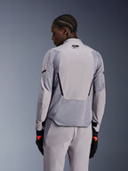 Kurtka Alpinestars Aeroshell Airflow w kolorze Mid Gray Anthracite, widok z tyłu prezentujący oddychające panele z siatki i perforacje laserowe, techniczna konstrukcja z elastycznego softshellu z wydłużonym panelem tylnym, sportowy styl z dopasowanymi szarymi spodniami i czarnymi rękawicami.
