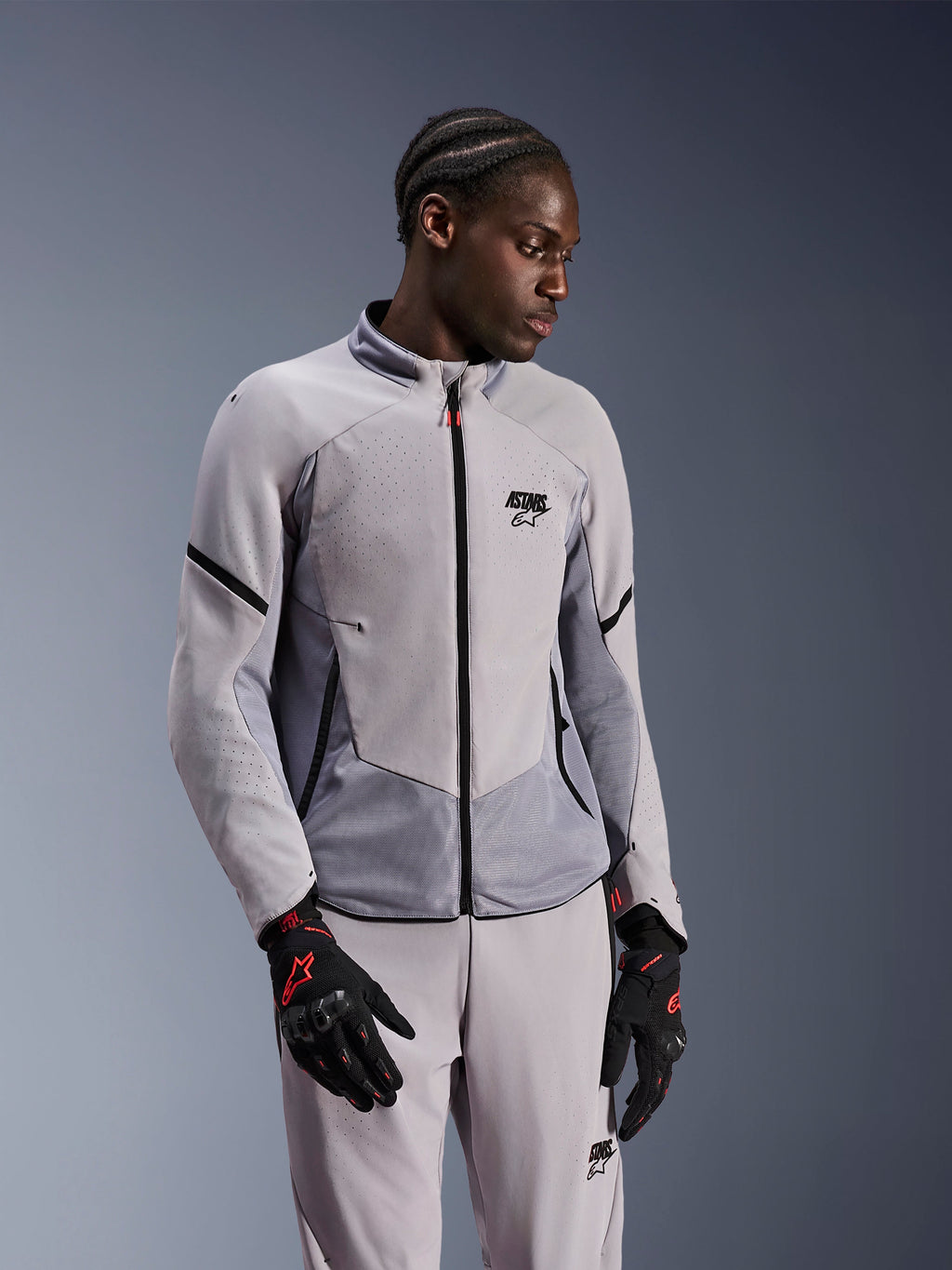 Kurtka Alpinestars Aeroshell Airflow, Mid Gray Anthracite, noszona przez modela z dopasowanymi spodniami tekstylnymi i czarnymi rękawicami z czerwonymi akcentami, laserowo perforowane strefy i panele z siatki dla lepszej wentylacji, smukły sportowy krój do jazdy motocyklowej