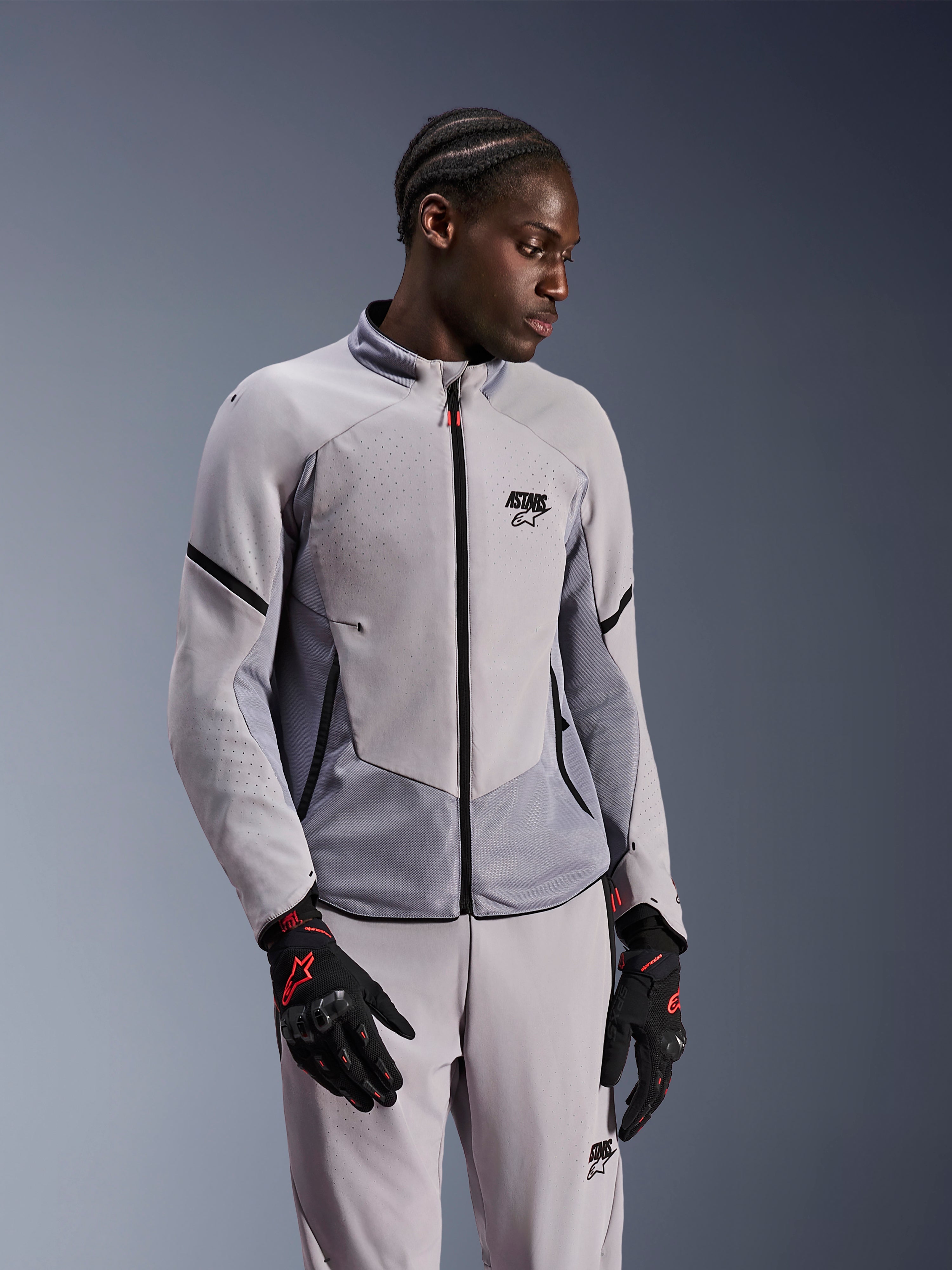 Kurtka Alpinestars Aeroshell Airflow, Mid Gray Anthracite, noszona przez modela z dopasowanymi spodniami tekstylnymi i czarnymi rękawicami z czerwonymi akcentami, laserowo perforowane strefy i panele z siatki dla lepszej wentylacji, smukły sportowy krój do jazdy motocyklowej