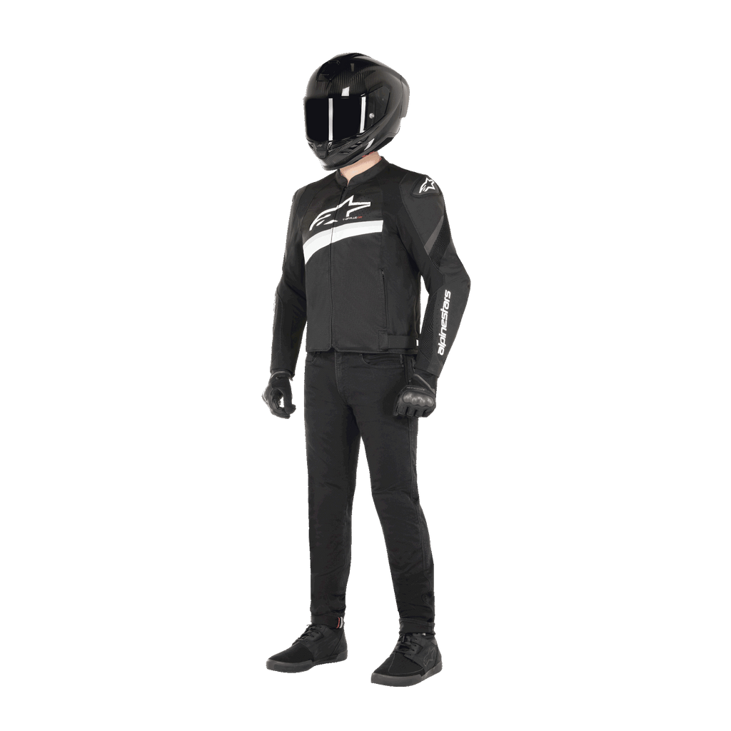 Motocyklista w kurtce Alpinestars T-GP Plus R V4 Airflow w kolorze czarno-białym, tekstylna kurtka motocyklowa z panelami z siatki i białym logo Alpinestars, w zestawie z czarnym kaskiem, czarnymi rękawicami motocyklowymi, czarnymi spodniami i czarnymi butami