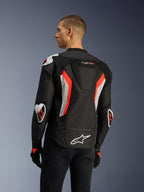 Kurtka Alpinestars T-GP Air w kolorze Black Red Fluo, widok z tyłu pod kątem trzech czwartych na modelu, podkreślający garb aerodynamiczny, zewnętrzne ochraniacze Racing GP DFS na ramionach i łokciach, laserowo perforowane panele mesh oraz białe i czerwone akcenty fluo, tekstylna kurtka motocyklowa o sportowym kroju.