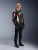 Kurtka Alpinestars T-GP Air, Black Red Fluo, noszona przez modela z czarnymi spodniami i rękawicami motocyklowymi, wyposażona w laserowo perforowane panele tekstylne, białe logo Alpinestars i czerwone akcenty, sportowa kurtka motocyklowa do jazdy szosowej w ciepłe dni
