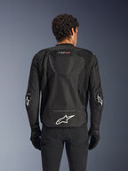 Alpinestars T-GP Air Jacket, Black, rear view of textile motorcycle jacket, featuring an aerodynamic hump, large mesh ventilation panels, and white Alpinestars logo on the lower back, styled with black motorcycle gloves and pants