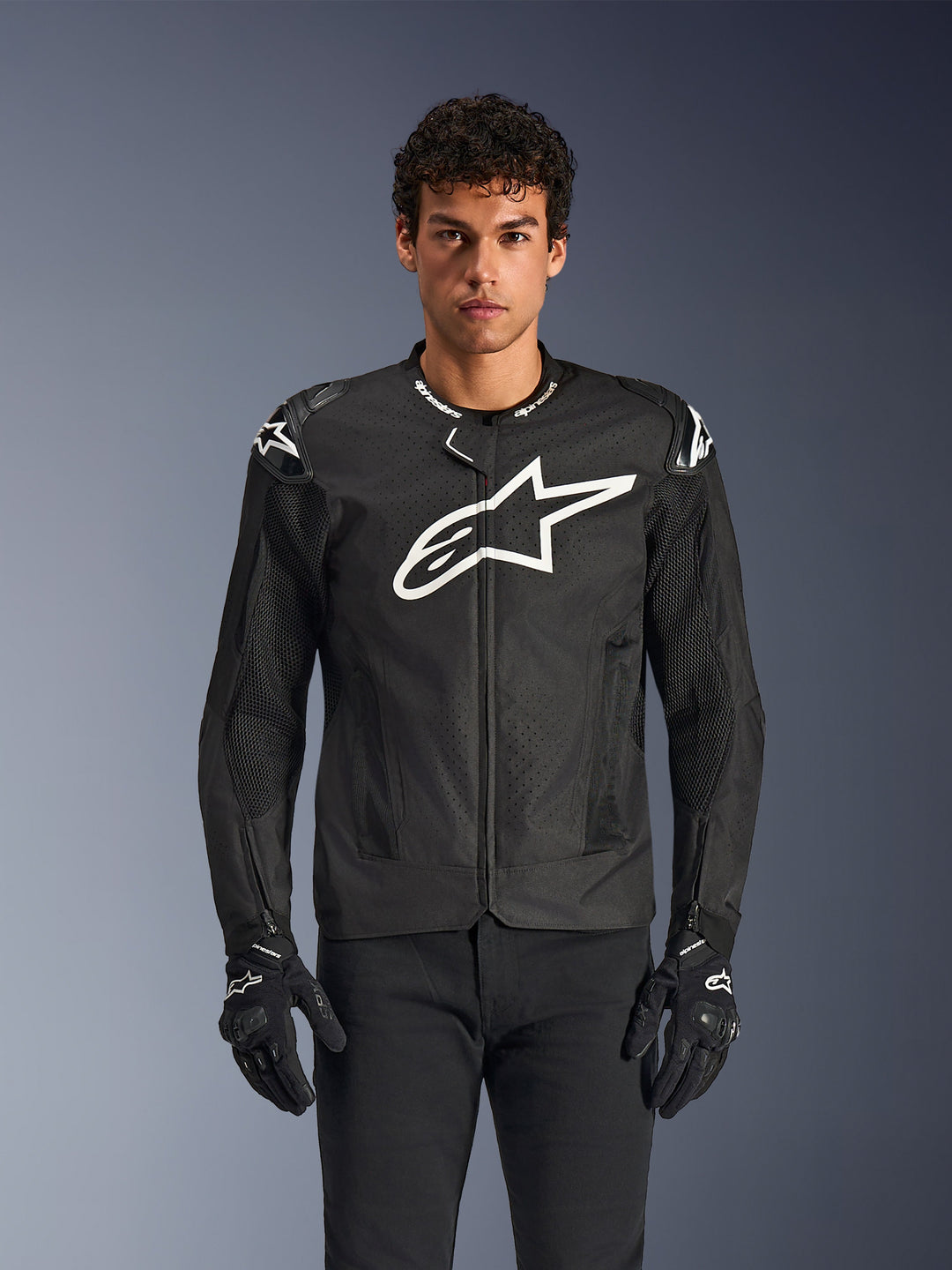 Alpinestars T-GP Air Jacket, Black motorcycle jacket with white logo, perforated ventilation panels, protective shoulder padding, worn with black and white gloves, sleek sporty design for street riding