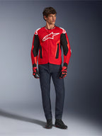 Kurtka Alpinestars T-GP Air, Bright Red Red Fluo Black, męski model w pełnym stroju motocyklowym z ciemnoniebieskimi dżinsami i pasującymi rękawicami, sportowa kurtka tekstylna z perforowanymi panelami z siatki i białym logo Astars, zdjęcie studyjne.