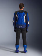 Alpinestars T-GP Air Jacket, jasnoniebieska, granatowa i biała, widok z tyłu prezentujący garb aerodynamiczny i siatkowe panele wentylacyjne, białe logo Alpinestars w dolnej części pleców, zestawiona z czarnymi spodniami i niebieskimi butami wyścigowymi