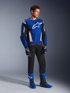 Kurtka Alpinestars T-GP Air, sportowa tekstylna kurtka motocyklowa, jaskrawoniebieska, granatowa i biała, noszona z pasującymi niebiesko-czarnymi rękawicami, czarnymi spodniami i niebieskimi butami wyścigowymi, białe logo na klatce piersiowej i techniczne panele z siatki, ujęcie studyjne całej sylwetki