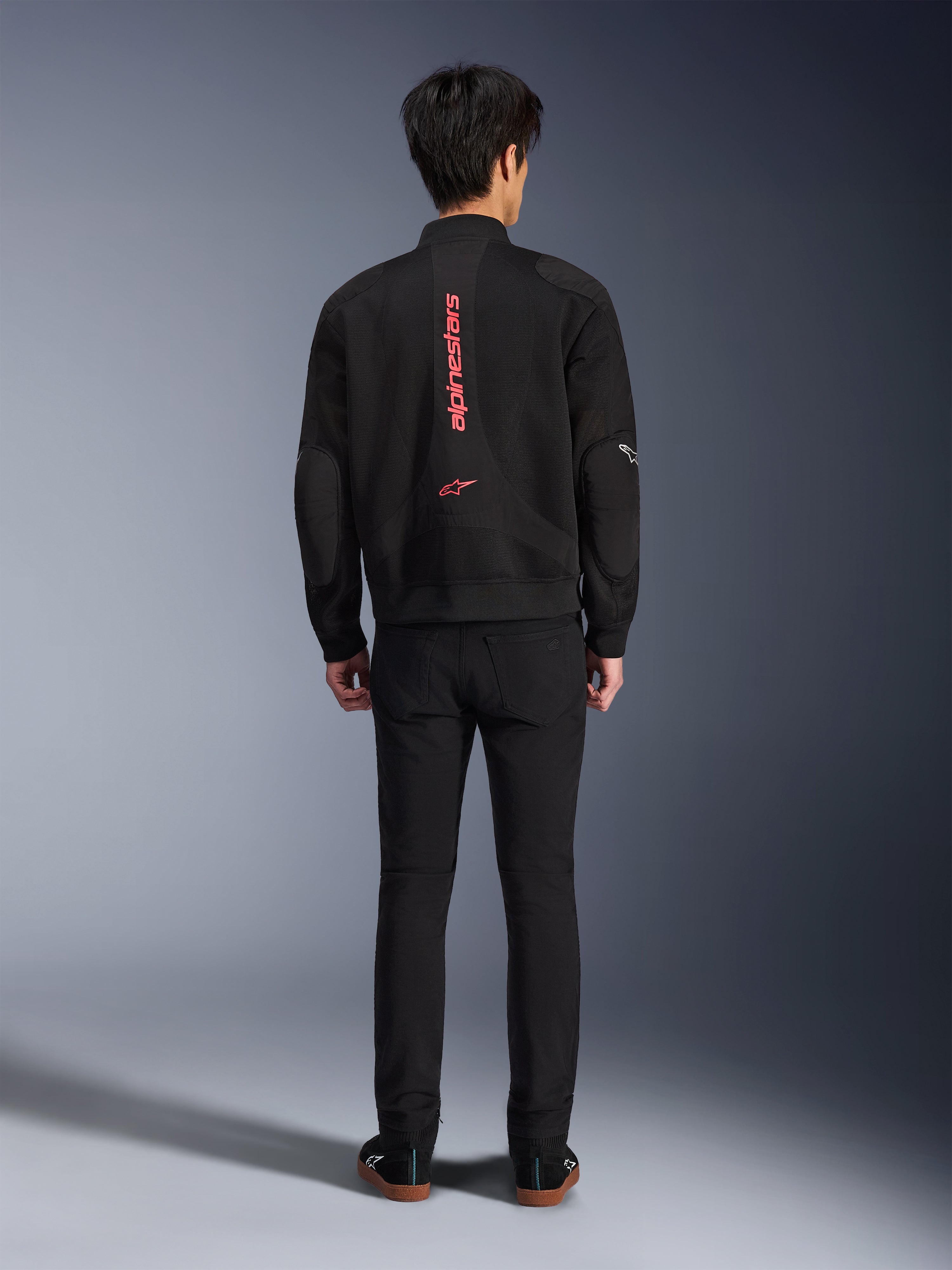 Kurtka Alpinestars Flight Air w kolorze Black Bright Red, widok z tyłu miejskiej kurtki motocyklowej typu bomber, z pionowym czerwonym napisem i logo Alpinestars na plecach, lekka konstrukcja z siatki 3D, zestawiona z czarnymi spodniami dla nowoczesnego wyglądu.