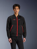 Alpinestars Flight Air Jacket w kolorze czarnym i jasnoczerwonym, miejska kurtka motocyklowa w stylu bomber noszona przez modela, z siatkowymi panelami wentylacyjnymi, wyrazistym czerwonym zamkiem błyskawicznym, czerwonymi detalami kieszeni i logo na piersi, zestawiona z czarnymi spodniami