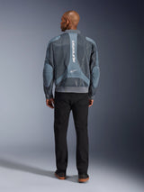 Kurtka Alpinestars Flight Air w kolorze Storm Gray, widok z tyłu na modela w miejskiej kurtce motocyklowej z panelami z siatki 3D i pionowym logo Alpinestars, w zestawieniu z czarnymi spodniami tworzącymi nowoczesny, miejski styl.