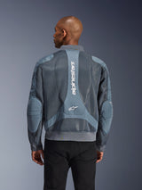 Alpinestars Flight Air Jacket w kolorze Storm Gray, widok z tyłu na modelu, miejska kurtka motocyklowa z rozszerzonymi panelami z siatki 3D, pionowym logo Alpinestars na plecach oraz ściągaczami u dołu i przy kołnierzu w stylu bomberki.