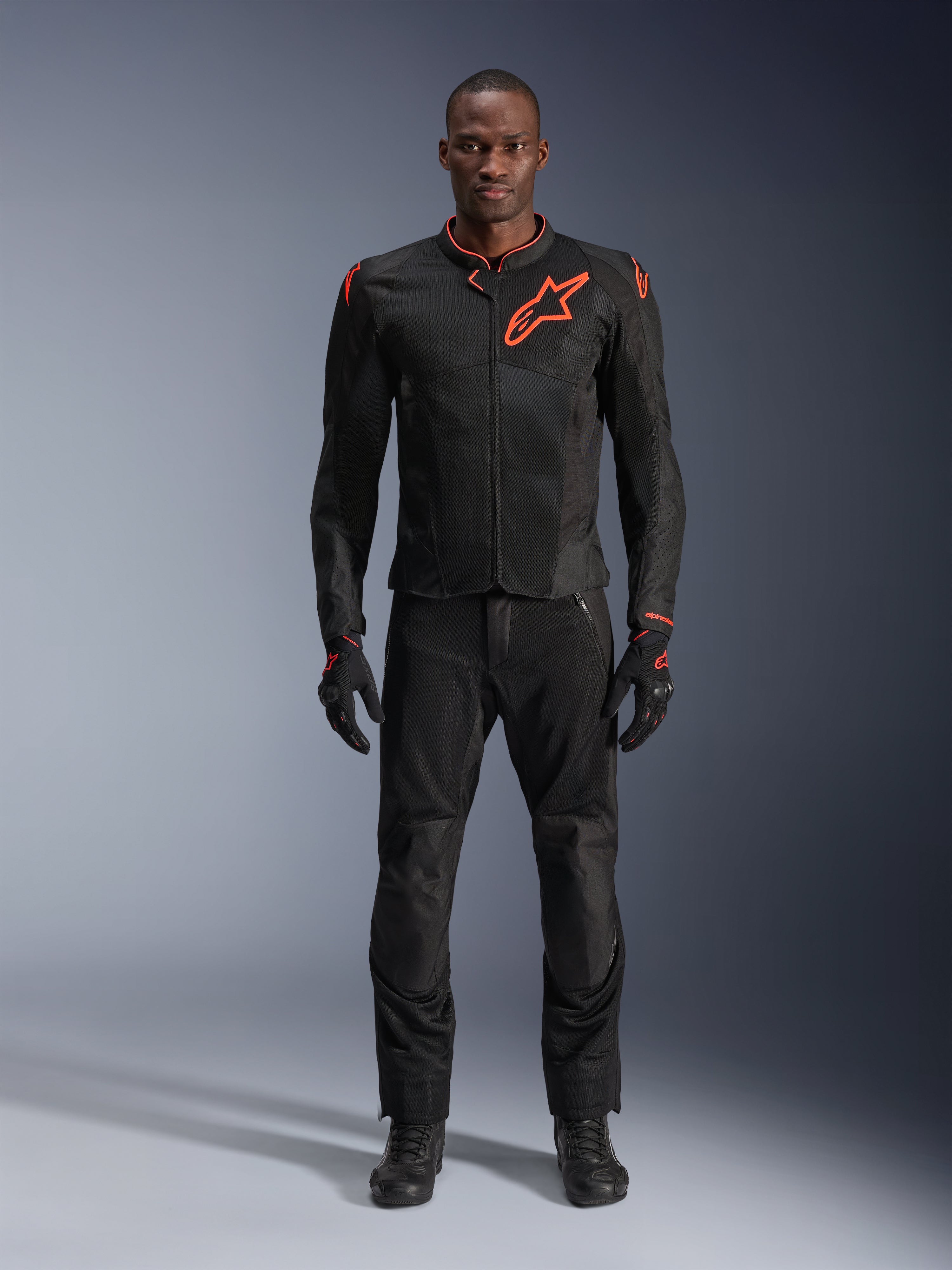 Alpinestars Viper Air V4 Jacket w kolorze Black Red Fluo, noszona przez modela z dopasowanymi czarnymi spodniami i rękawicami, z panelami z siatki dla lepszego przepływu powietrza i wyraźnym czerwonym logo Alpinestars na klatce piersiowej, sportowa odzież motocyklowa.