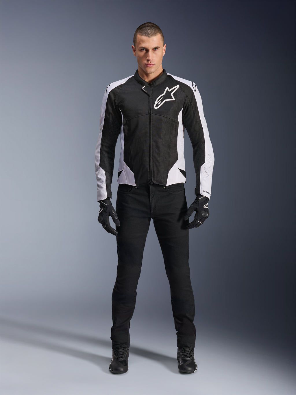 Kurtka Alpinestars Viper Air V4, czarno-biała kurtka motocyklowa z dużym białym logo na klatce piersiowej, noszona przez modela w czarnych spodniach i rękawicach, panele siatkowe zapewniające wentylację, sportowa odzież do jazdy szosowej