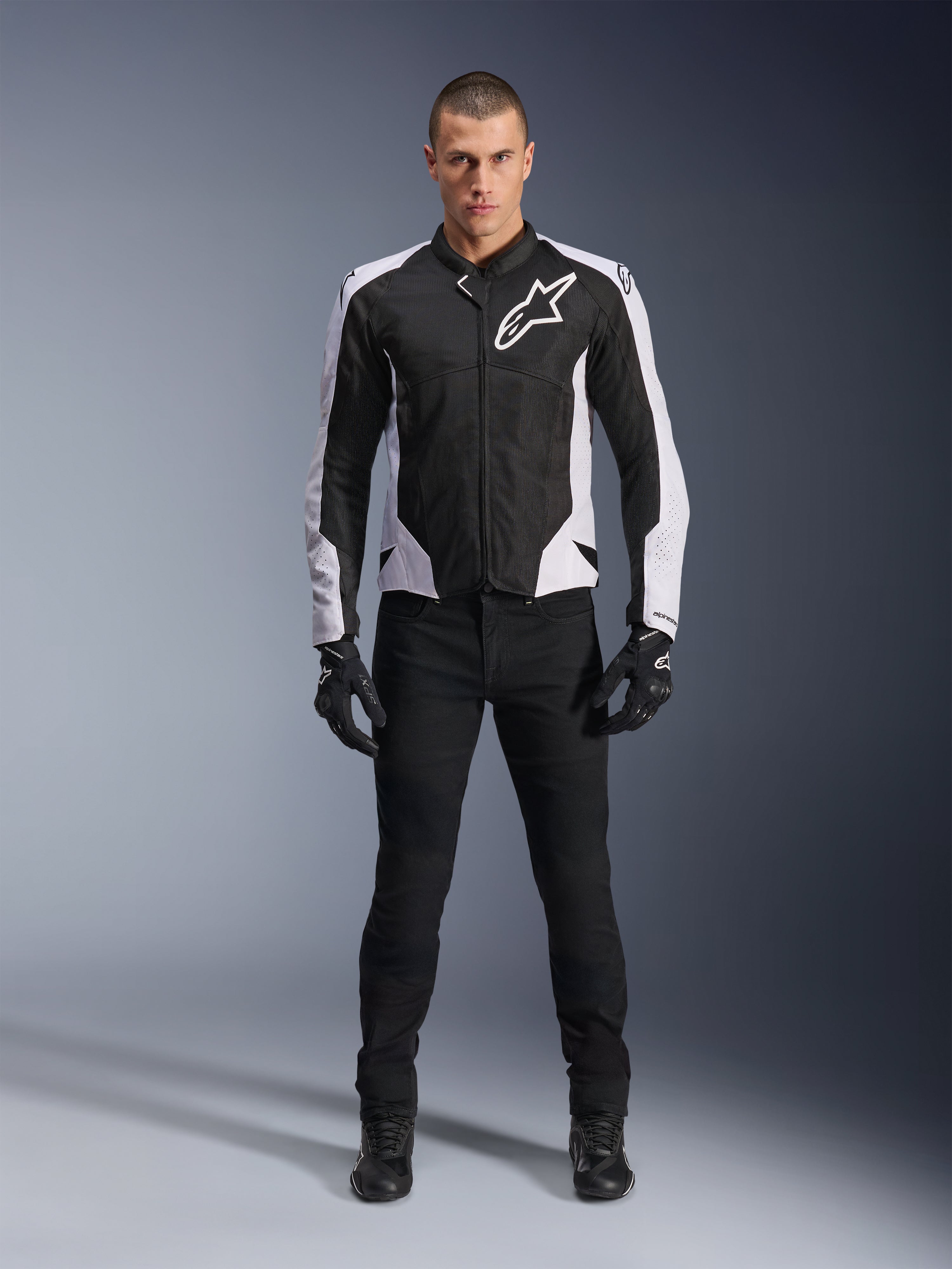 Kurtka Alpinestars Viper Air V4, czarno-biała kurtka motocyklowa z dużym białym logo na klatce piersiowej, noszona przez modela w czarnych spodniach i rękawicach, panele siatkowe zapewniające wentylację, sportowa odzież do jazdy szosowej