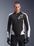Alpinestars Viper Air V4 Jacket, motocyklowa kurtka wyścigowa, czarno-biała, noszona przez motocyklistę, konstrukcja z technicznej siatki i materiału tekstylnego z białymi panelami na ramionach, wyraźne logo gwiazdy na klatce piersiowej, sportowy design, w zestawieniu z czarnymi rękawicami motocyklowymi
