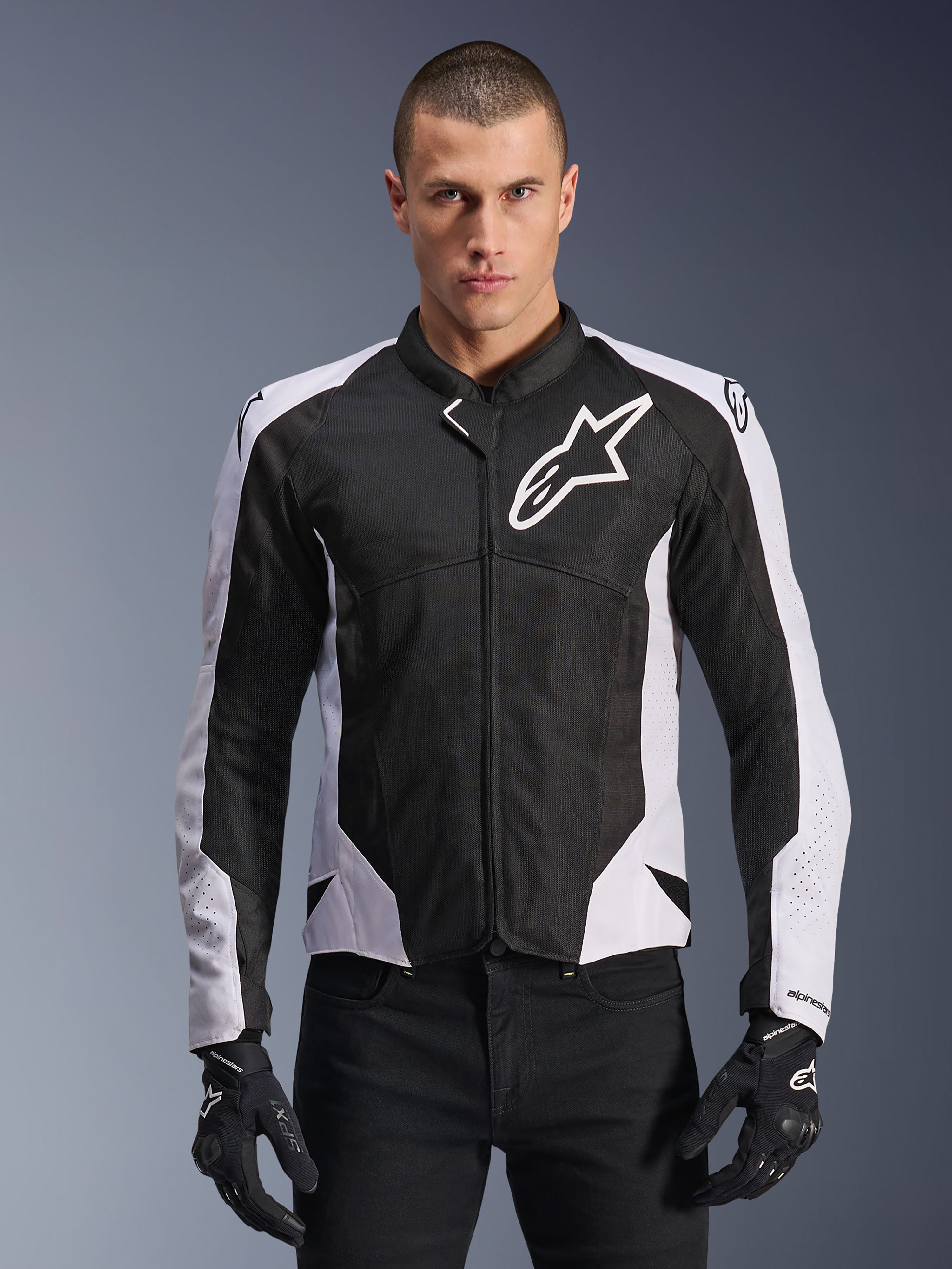 Alpinestars Viper Air V4 Jacket, motocyklowa kurtka wyścigowa, czarno-biała, noszona przez motocyklistę, konstrukcja z technicznej siatki i materiału tekstylnego z białymi panelami na ramionach, wyraźne logo gwiazdy na klatce piersiowej, sportowy design, w zestawieniu z czarnymi rękawicami motocyklowymi