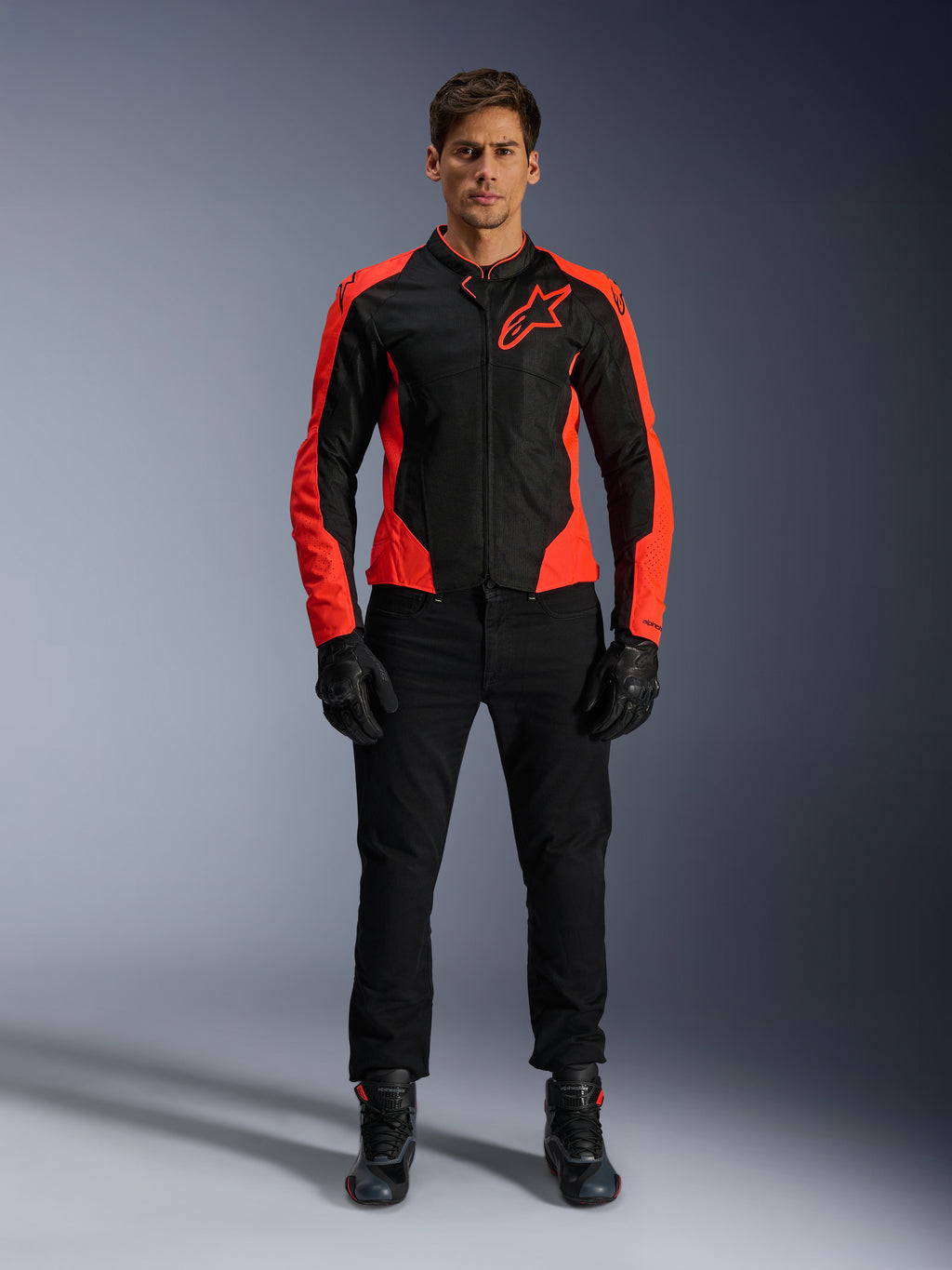 Męski model w kurtce Alpinestars Viper Air V4 w kolorze Red Fluo i czarnym, w zestawieniu z czarnymi spodniami, rękawicami i butami motocyklowymi, z oddychającymi panelami z siatki dla wentylacji i wyraźnym logo gwiazdy na piersi, sportowa odzież motocyklowa szosowa