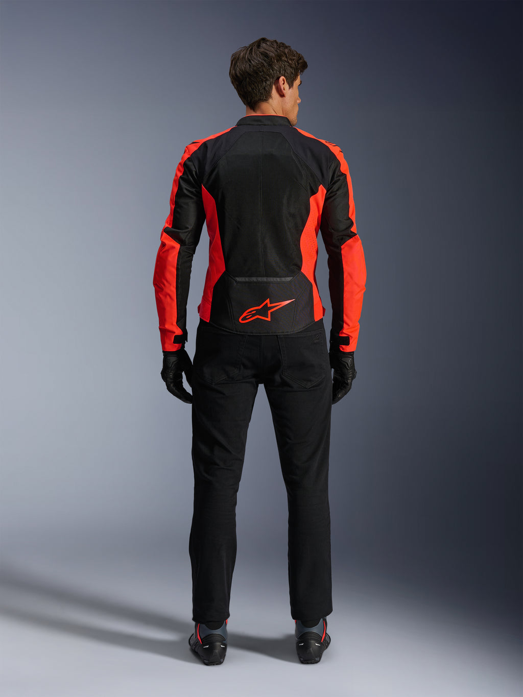 Kurtka Alpinestars Viper Air V4, czerwona fluorescencyjna i czarna, widok od tyłu ukazujący duże panele z siatki technologicznej i jaskrawoczerwone akcenty boczne, czerwone logo Alpinestars na dole pleców, noszona z czarnymi spodniami motocyklowymi i rękawicami