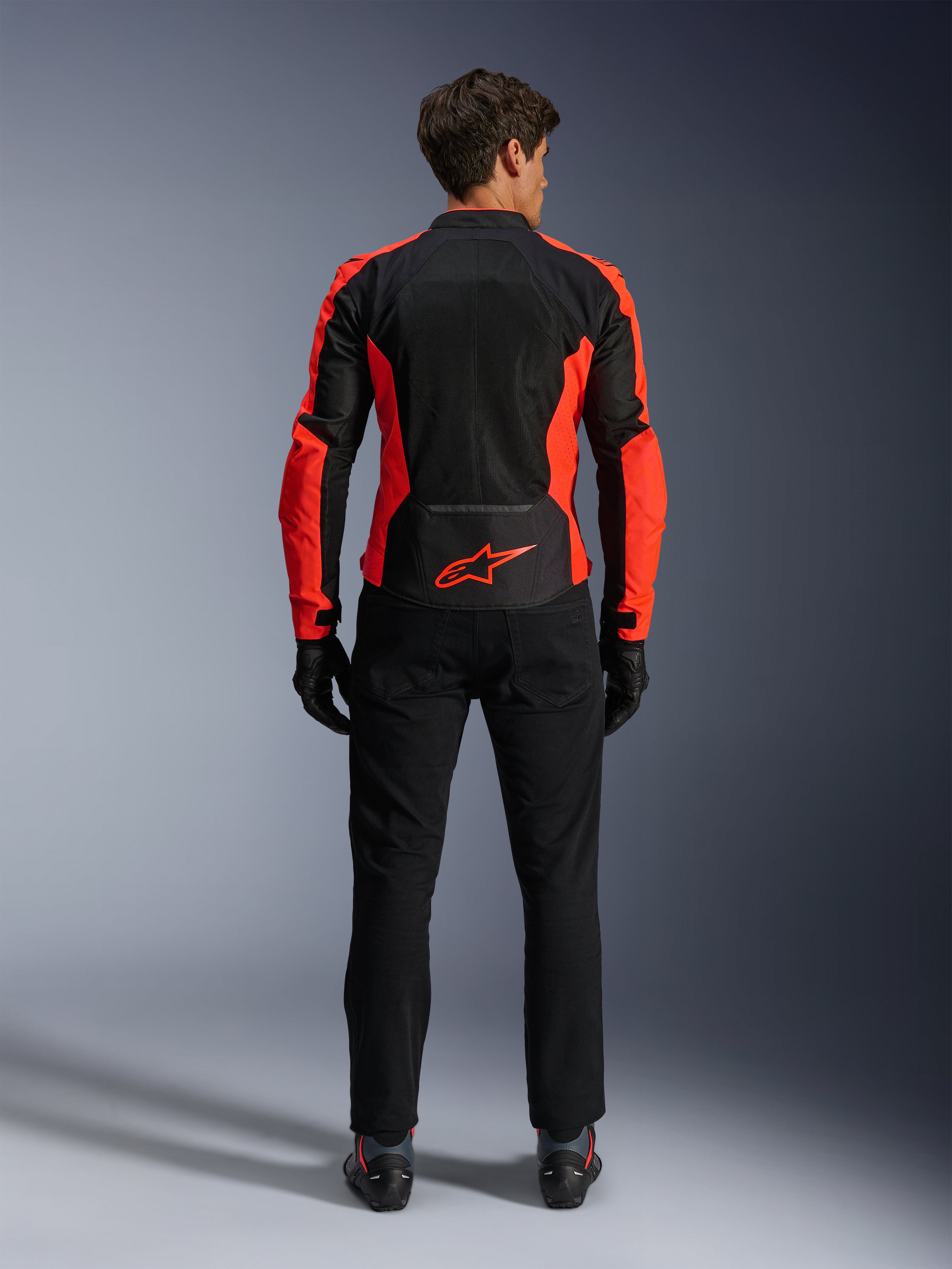 Kurtka Alpinestars Viper Air V4, czerwona fluorescencyjna i czarna, widok od tyłu ukazujący duże panele z siatki technologicznej i jaskrawoczerwone akcenty boczne, czerwone logo Alpinestars na dole pleców, noszona z czarnymi spodniami motocyklowymi i rękawicami