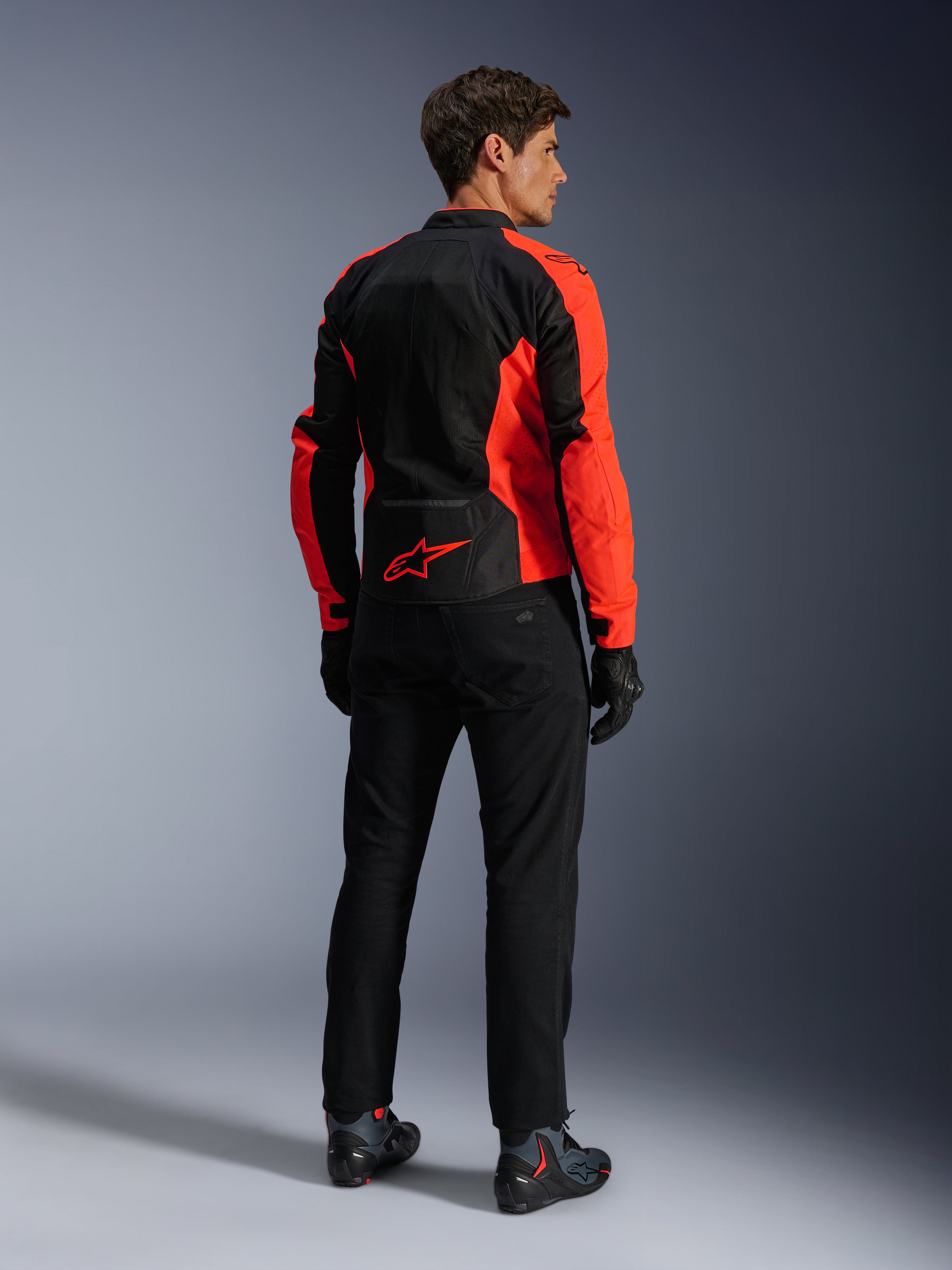 Kurtka Alpinestars Viper Air V4, kolor neonowy czerwony i czarny, widok z tyłu na modelu, wyposażona w panele z siatki technicznej i czerwone logo gwiazdy na dole pleców, zestawiona z czarnymi spodniami motocyklowymi i rękawicami, kompletny zestaw szosowy.