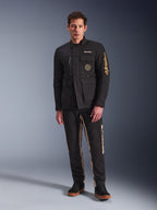 Męski model w kurtce Alpinestars Dice Jacket, czarna miejska kurtka motocyklowa w stylu vintage field jacket, cztery funkcjonalne kieszenie z przodu, branding Alpinestars na rękawie i piersi, zestawiona z czarno-beżowymi spodniami, nowoczesna miejska odzież motocyklowa