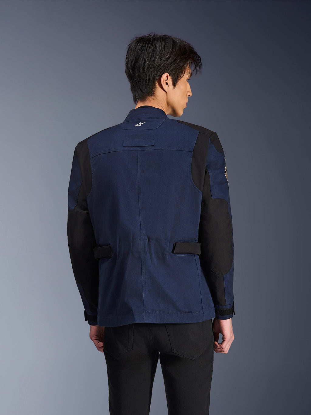 Alpinestars Dice Jacket, ciemnoniebieska i czarna miejska motocyklowa kurtka terenowa, widok z tyłu, noszona przez mężczyznę, wzmocnione czarne panele na ramionach i łokciach, regulowane patki w talii