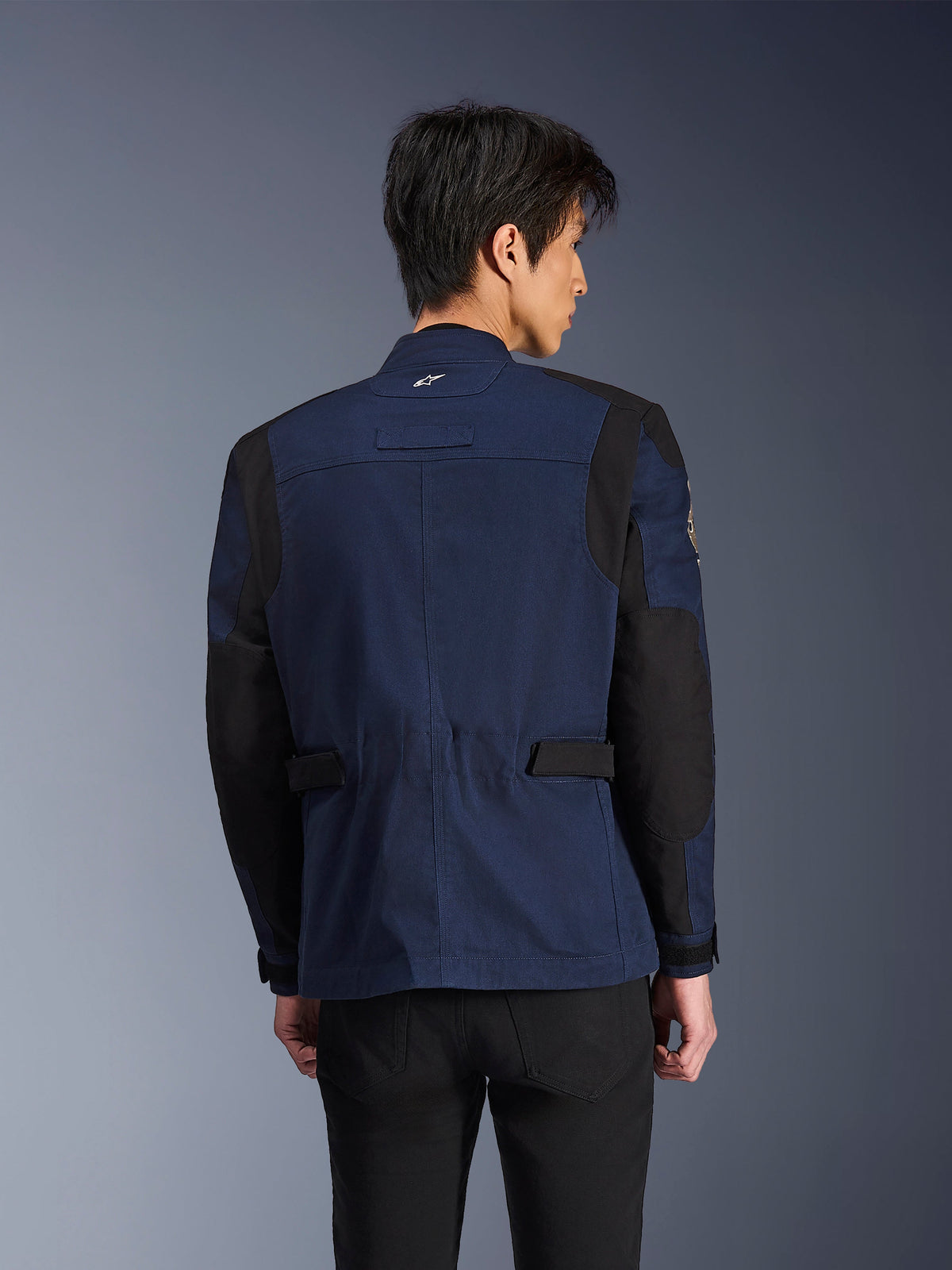 Alpinestars Dice Jacket, ciemnoniebieska i czarna miejska motocyklowa kurtka terenowa, widok z tyłu, noszona przez mężczyznę, wzmocnione czarne panele na ramionach i łokciach, regulowane patki w talii