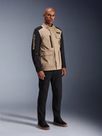 Alpinestars Dice Jacket, miejska kurtka motocyklowa, czarno-piaskowa, dwukolorowy design z czarnymi rękawami i korpusem w kolorze khaki, noszona przez modela w czarnych spodniach i czarnych butach sportowych, estetyka inspirowana odzieżą roboczą z kieszeniami użytkowymi i haftowanym logo na rękawie.