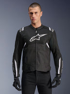Alpinestars T-SPS Air V2 Jacket, tekstylna kurtka motocyklowa, czarna z białymi akcentami, duże białe logo na piersi, perforowana konstrukcja z siatki dla wentylacji, noszona z czarnymi spodniami i rękawicami