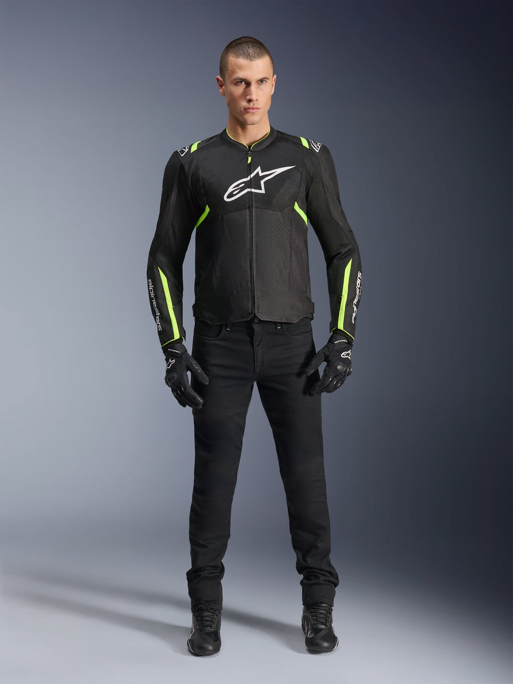 Kurtka Alpinestars T-Sps Air V2, czarna i żółta fluo, tekstylna kurtka motocyklowa z panelami z siatki, prezentowana przez modela w czarnych spodniach i rękawicach, białe logo Alpinestars na piersi, miejska sportowa odzież motocyklowa