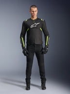 Kurtka Alpinestars T-Sps Air V2, czarna i żółta fluo, tekstylna kurtka motocyklowa z panelami z siatki, prezentowana przez modela w czarnych spodniach i rękawicach, białe logo Alpinestars na piersi, miejska sportowa odzież motocyklowa