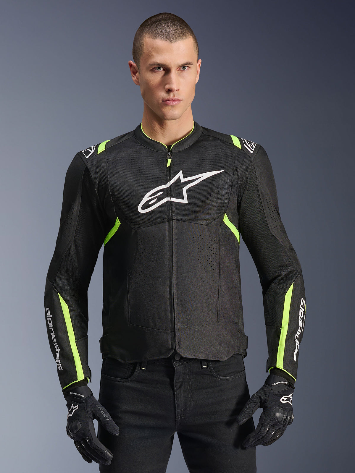 Alpinestars T-Sps Air V2 Jacket w kolorze czarno-żółtym neonowym, męski model ubrany w wentylowaną kurtkę tekstylną z panelami z siatki i białym logo na piersi, czarne rękawice motocyklowe, miejska odzież motocyklowa