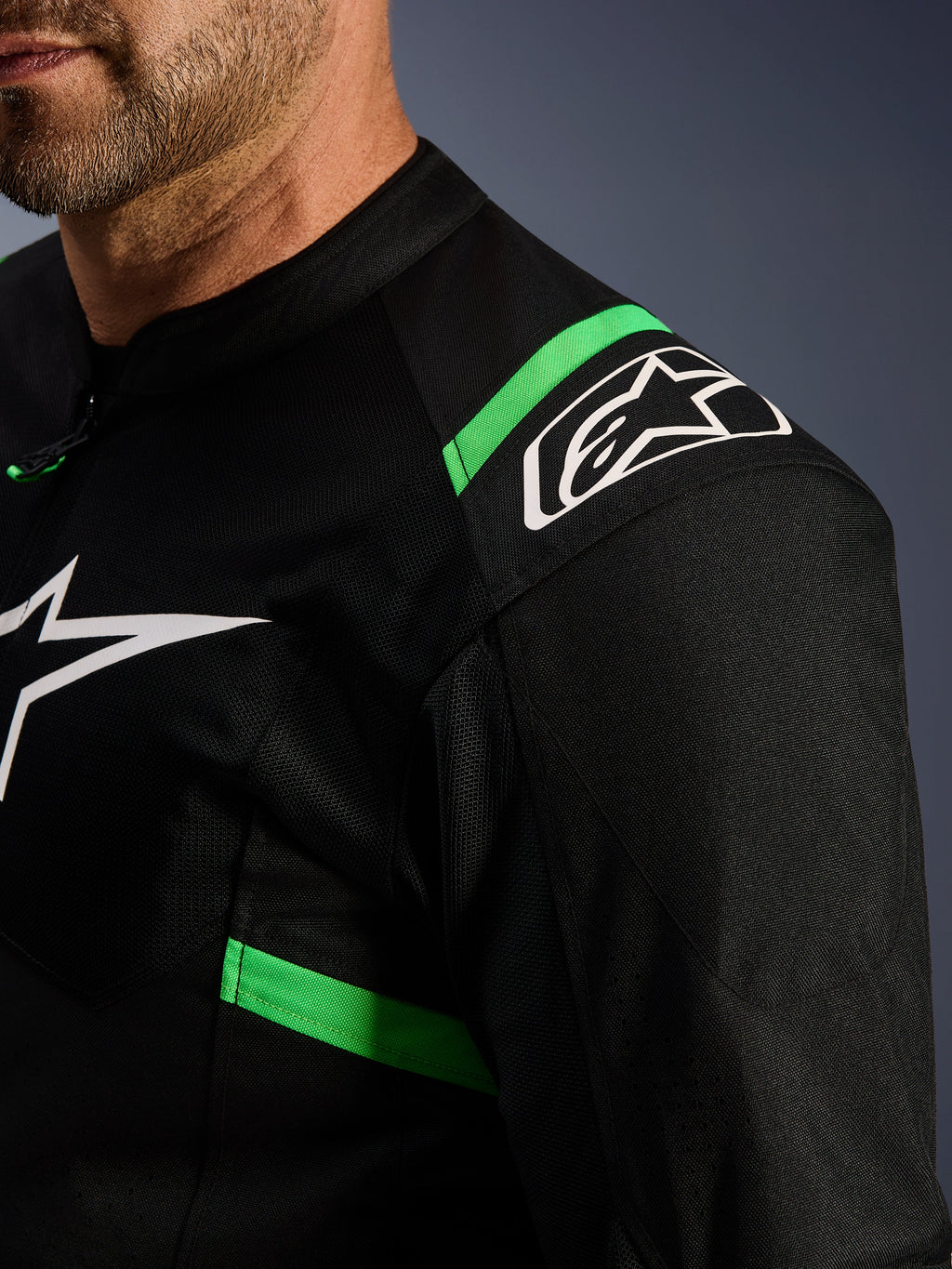 Alpinestars T-SPS Air V2 Jacket, czarna z neonowo-zielonymi elementami, zbliżenie na ramię i klatkę piersiową, białe logo z gwiazdą Alpinestars, techniczna tkanina siatkowa zapewniająca przepływ powietrza, sportowa kurtka motocyklowa