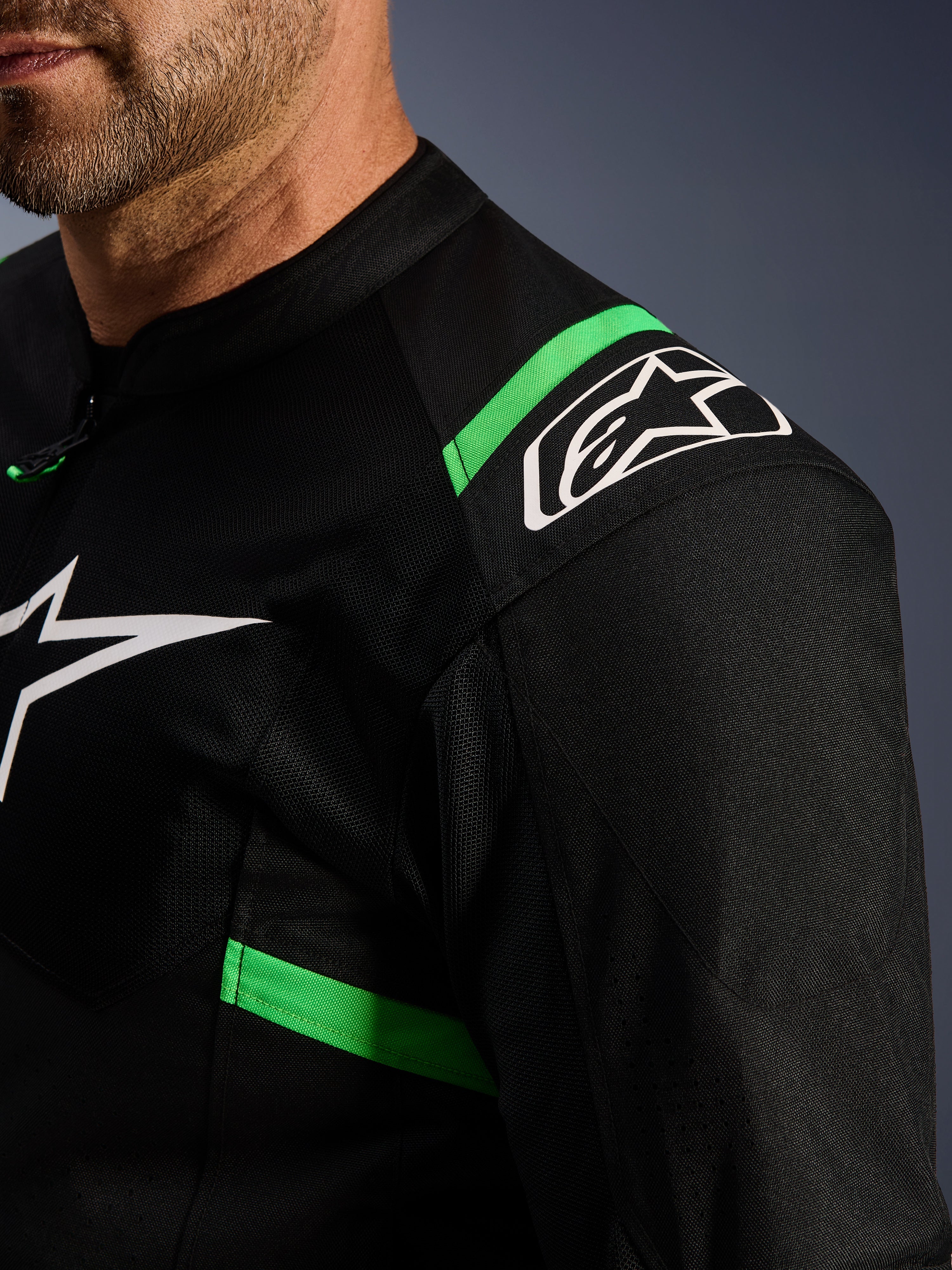 Alpinestars T-SPS Air V2 Jacket, czarna z neonowo-zielonymi elementami, zbliżenie na ramię i klatkę piersiową, białe logo z gwiazdą Alpinestars, techniczna tkanina siatkowa zapewniająca przepływ powietrza, sportowa kurtka motocyklowa