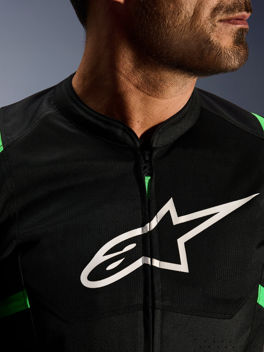 Zbliżenie na kurtkę Alpinestars T-SPS Air V2, czarno-zielona (Fluo Green), z oddychającymi panelami tech mesh, centralnym zamkiem i wyraźnym białym logo gwiazdy Alpinestars na klatce piersiowej, wyczynowa odzież motocyklowa