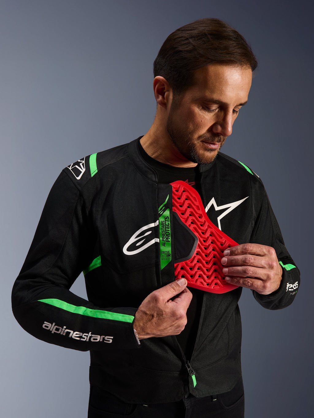 Kurtka Alpinestars T-SPS Air V2, kurtka motocyklowa czarno-zielona fluo, mężczyzna prezentujący czerwoną wkładkę ochronną klatki piersiowej Nucleon, etykieta Tech-Air Ready, sportowy design tekstylny z panelami z siatki