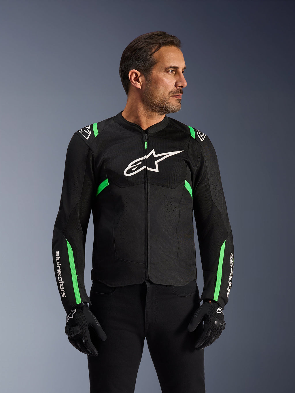 Kurtka motocyklowa Alpinestars T-SPS Air V2, czarna z neonową zielenią, noszona przez modela w czarnych rękawicach i spodniach, białe logo Alpinestars na piersi, neonowe zielone akcenty na ramionach i rękawach, panele z siatki technicznej dla wentylacji, sportowy krój do jazdy miejskiej