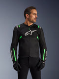 Kurtka motocyklowa Alpinestars T-SPS Air V2, czarna z neonową zielenią, noszona przez modela w czarnych rękawicach i spodniach, białe logo Alpinestars na piersi, neonowe zielone akcenty na ramionach i rękawach, panele z siatki technicznej dla wentylacji, sportowy krój do jazdy miejskiej
