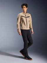 Alpinestars Bruiser Jacket, miejska kurtka motocyklowa, piaskowa, prezentowana przez modela w czarnych spodniach typu slim i czarnych trampkach, tekstylna konstrukcja inspirowana odzieżą roboczą z czarnymi akcentami suwaków, współczesny miejski styl uliczny.